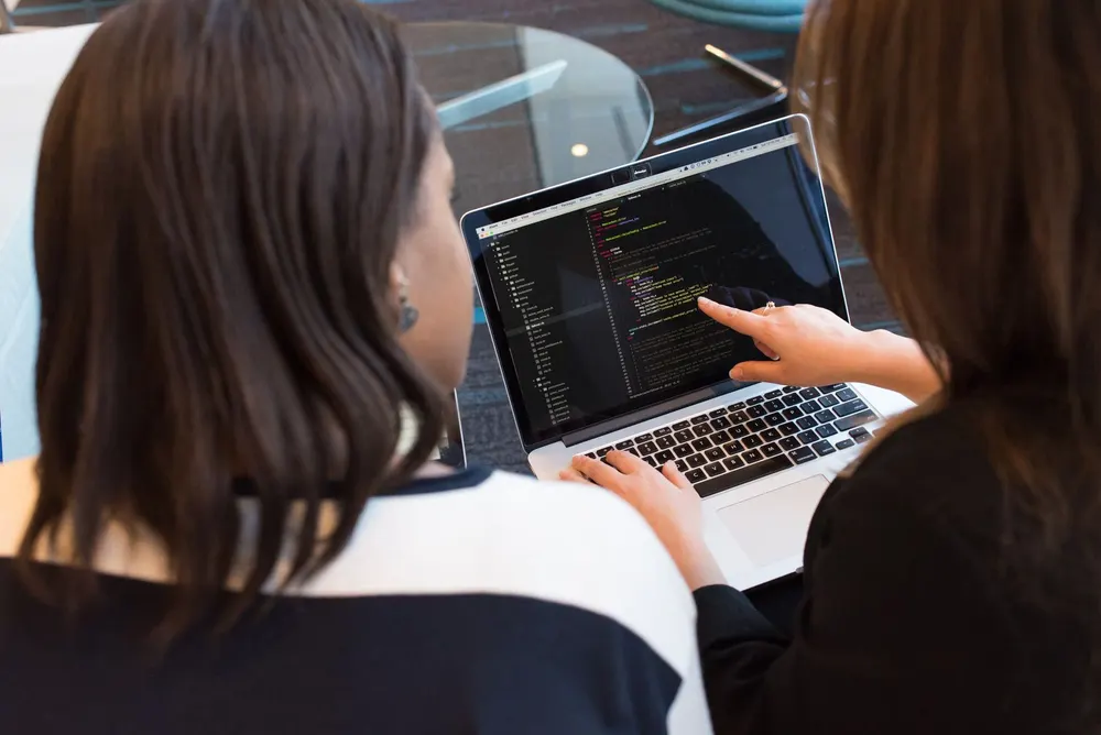 Two website professionals reviewing code on a laptop during a redesign project.